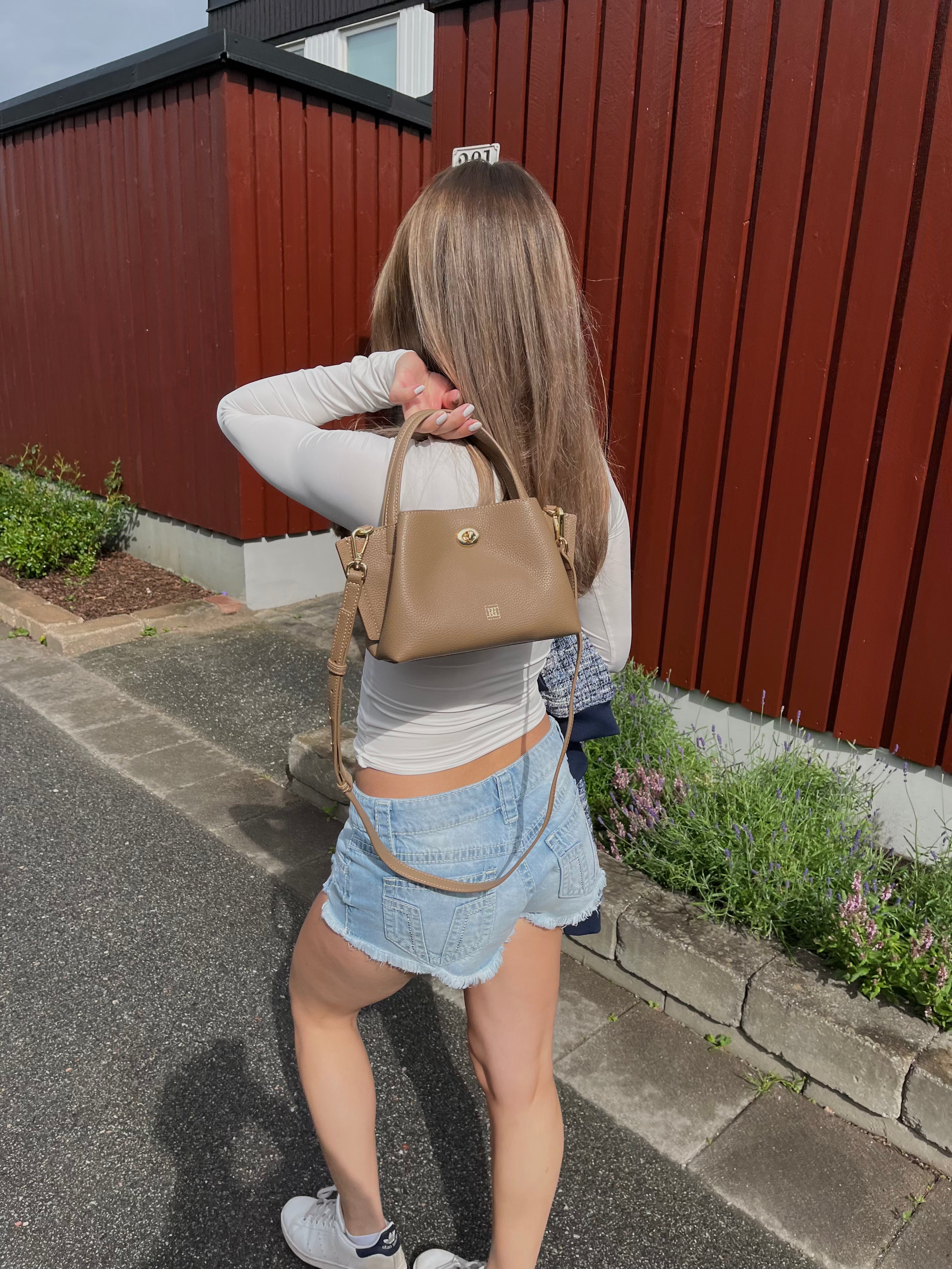A girl walking on a street holding a mini bag.