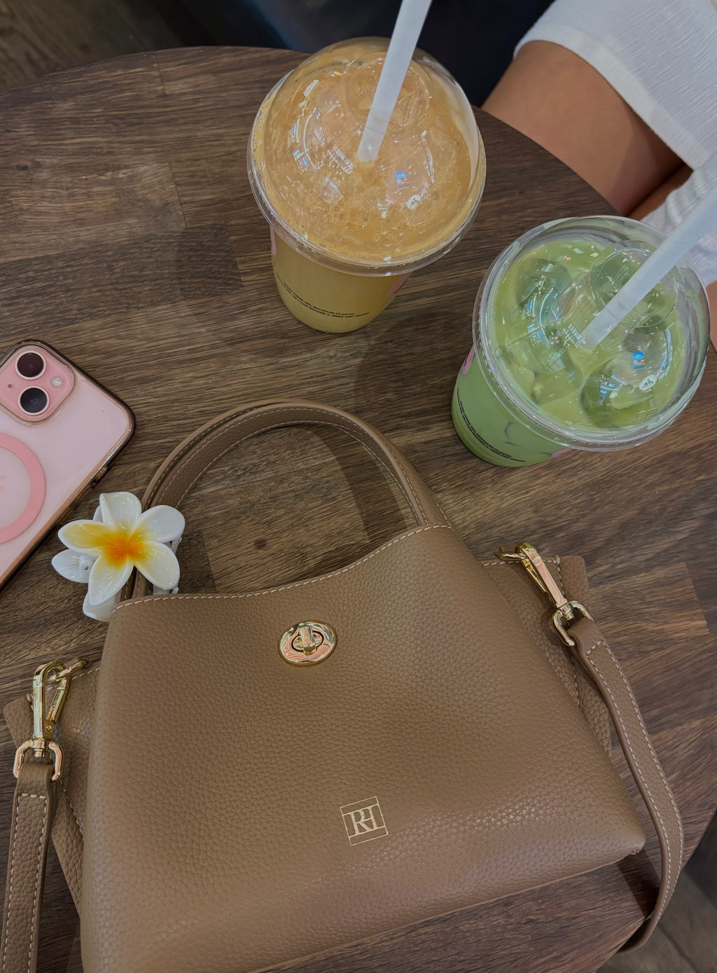 A mini bag on a wooden table with two drinks and a phone.